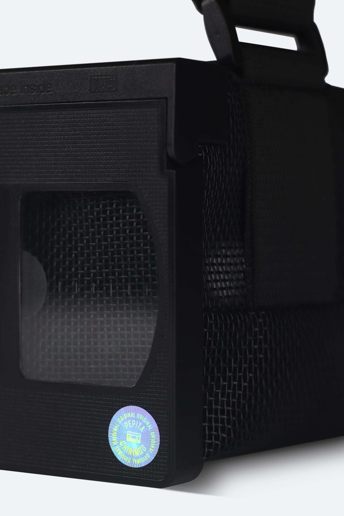 Close-up of the front detail of the black VHS handbag from the Videoclub 2025 Collection by Pepita Chiringo, showcasing the holographic sticker label, reminiscent of classic VHS tapes, adding a nostalgic touch to this handmade, sustainable fashion accessory.